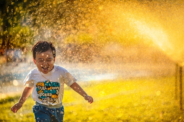 a smiling boy runs through spray of water