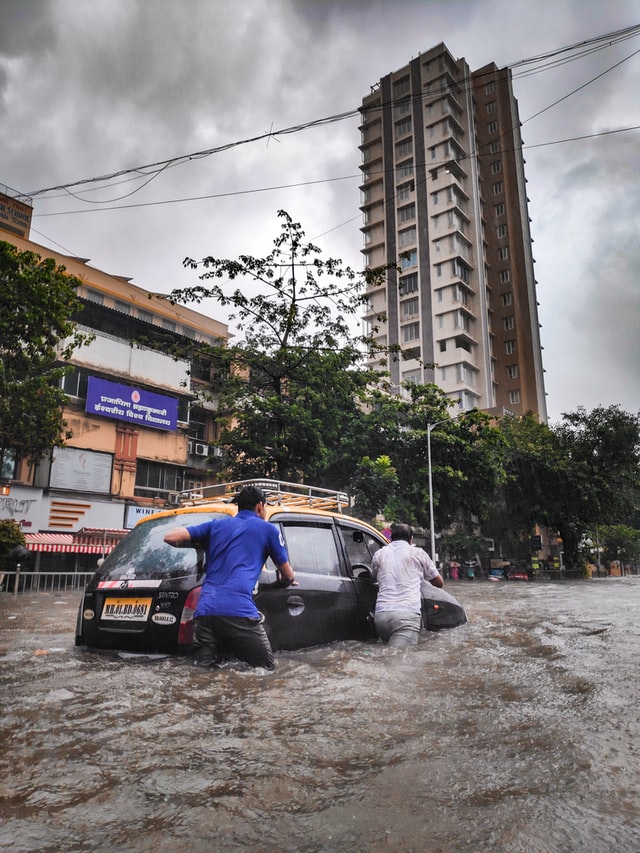 people push a car through flooded street